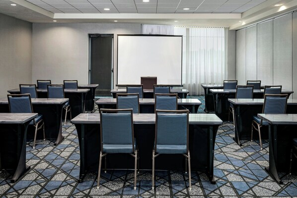 A conference room with tables and chairs, a large screen, and a door. - Courtyard by Marriott Richland - Columbia Point (Richland)