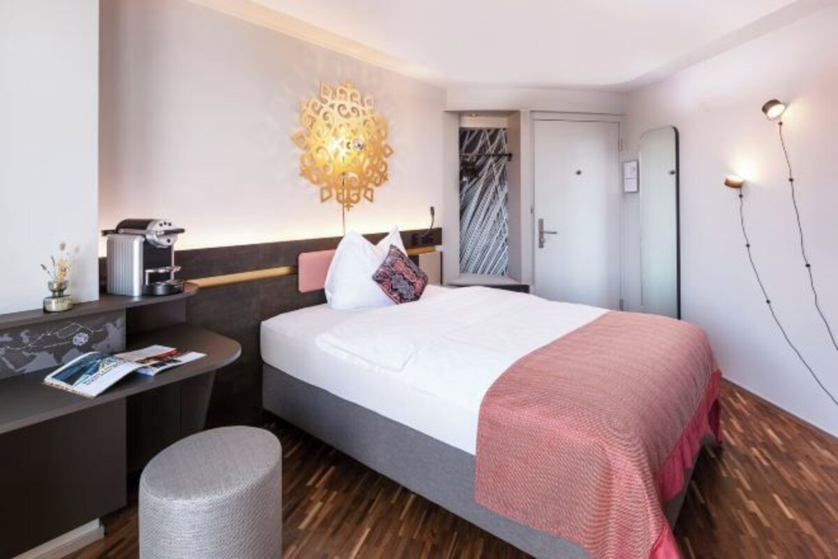Ett modernt hotellrum med en säng, ett nattduksbord och ett skrivbord med en stol.