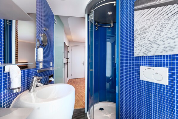 A modern bathroom with a large white sink, a glass-enclosed shower, and blue-tiled walls. - Lifestyle Hotel Sedartis Lake Zurich (Thalwil)