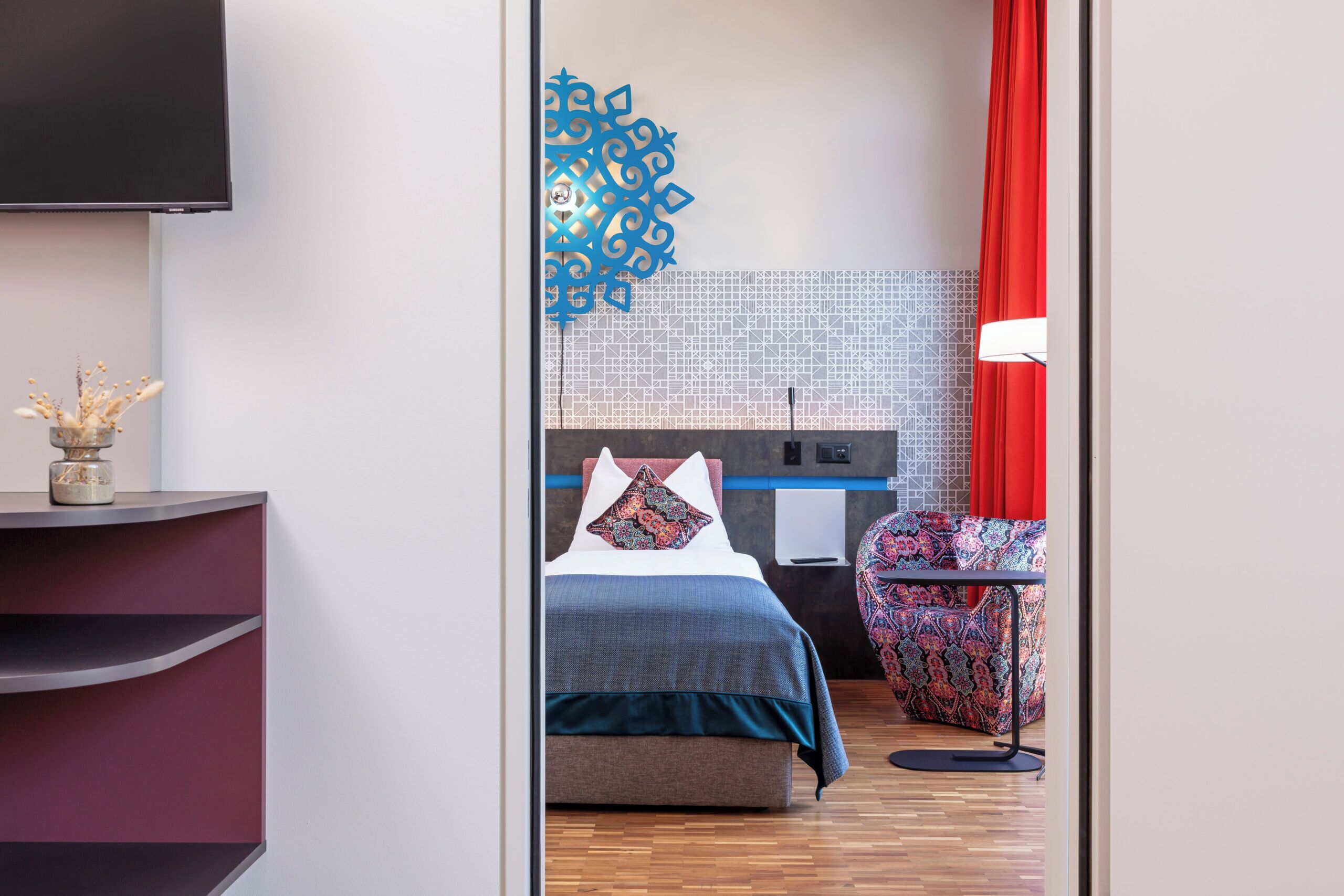 A modern hotel room with a bed, a desk, a chair, and a TV.