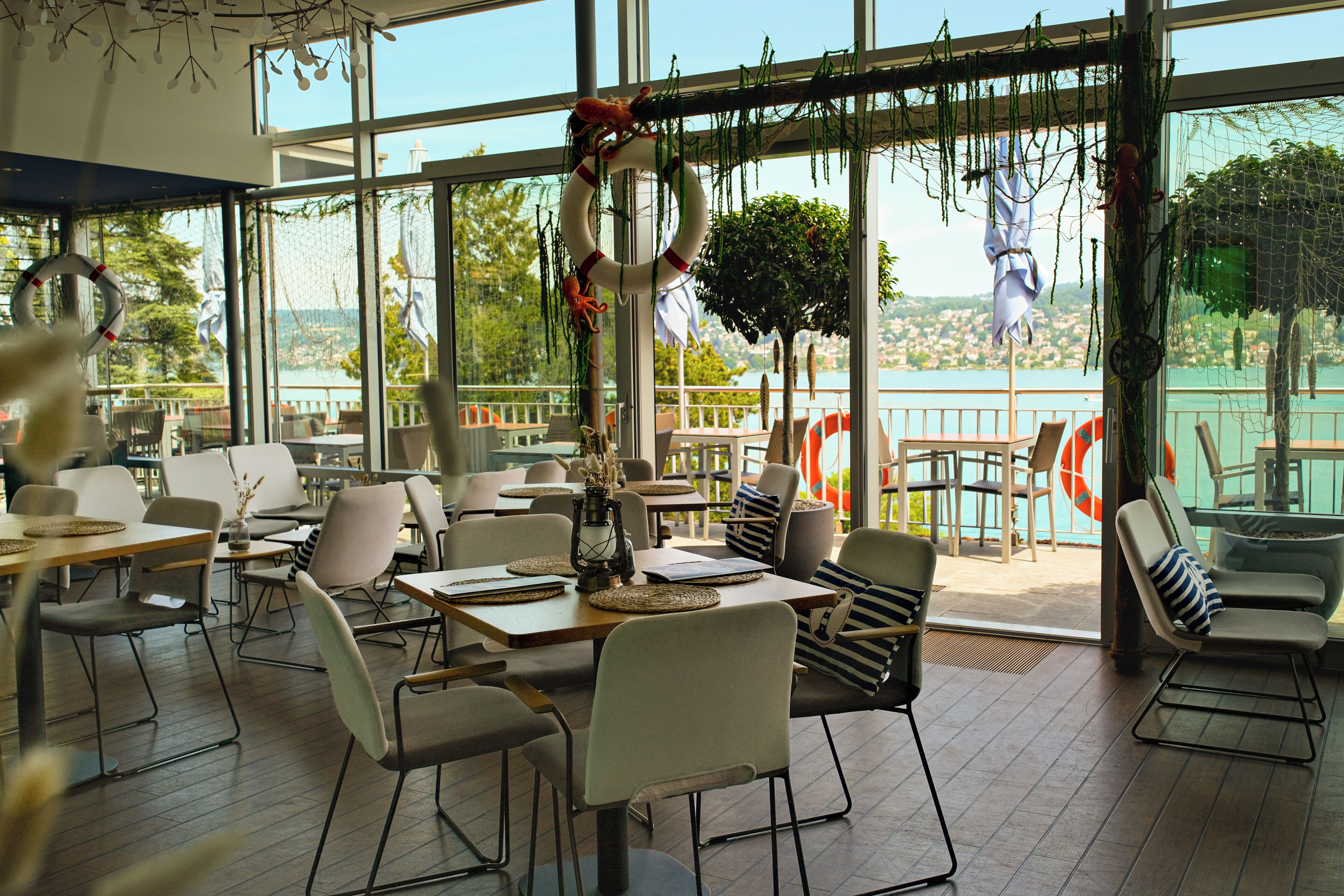 A restaurant with a view of a lake, featuring tables and chairs arranged for dining.