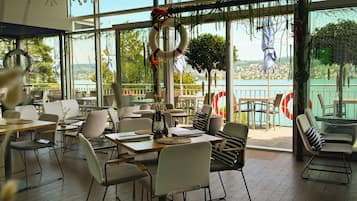 A restaurant with a view of a lake, featuring tables and chairs arranged for dining.