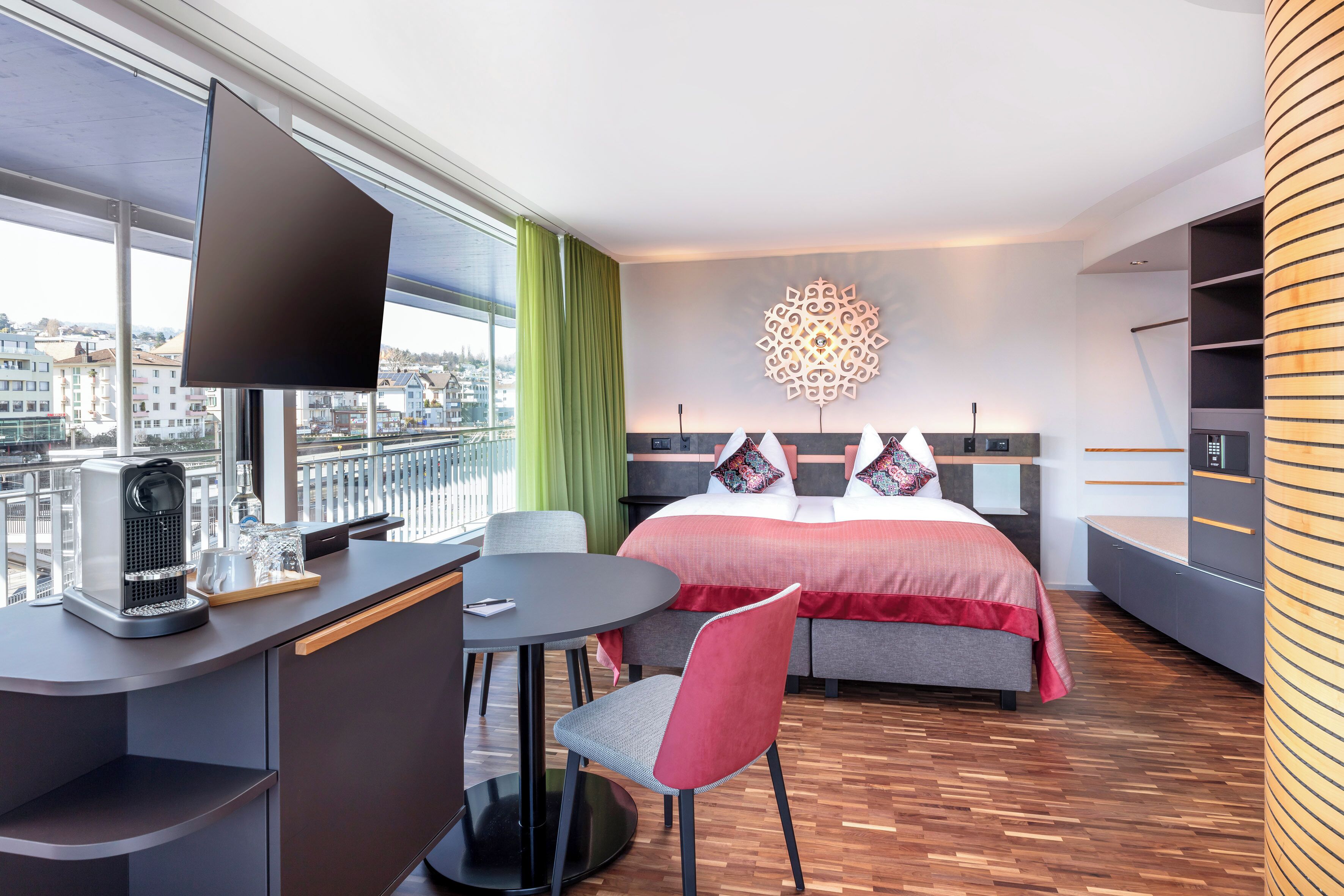A modern hotel room with a large bed, a desk with a coffee maker, a round table, and a chair.