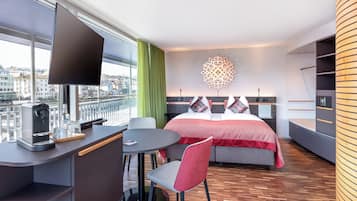 A modern hotel room with a large bed, a desk with a coffee maker, a round table, and a chair.