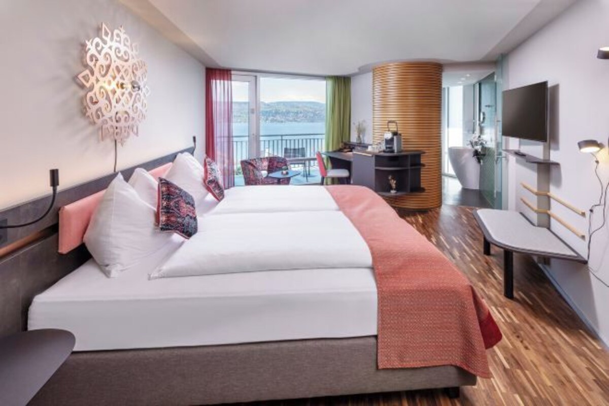 Ett hotellrum med två sängar, ett skrivbord, en stol, en TV och en balkong med utsikt.