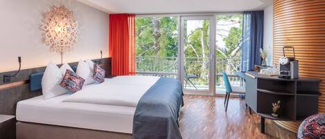 A modern hotel room with a bed, a desk, and a balcony with a view of trees.