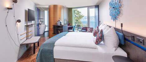 A modern hotel room with a large bed, a desk, and a view of the sea.