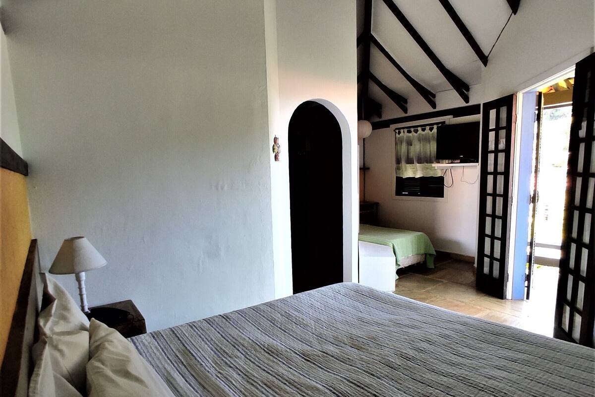 A bedroom with a bed, a nightstand, a lamp, a TV, and a view of another room.