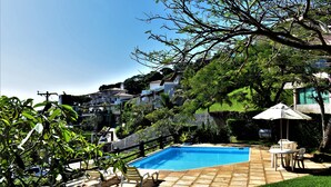 A swimming pool with a tiled deck, surrounded by greenery and a view of residential buildings. - Hibiscus Beach Pousada (Búzios)