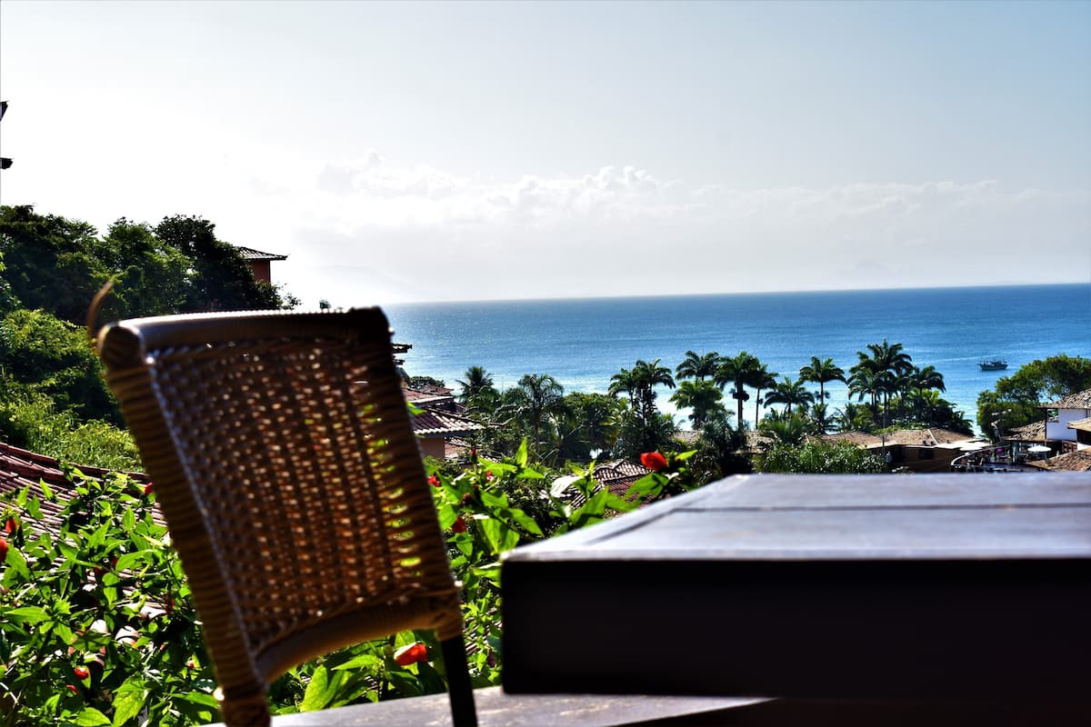 A wicker chair overlooking a coastal view with palm trees and a clear sky.