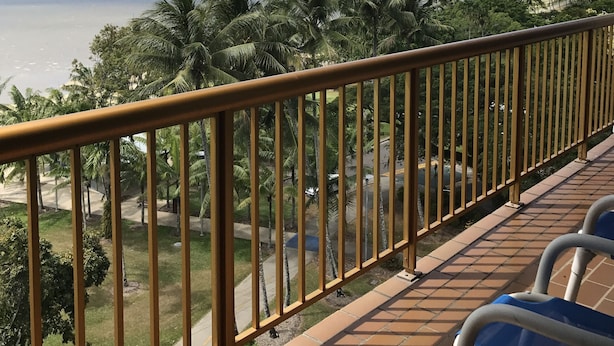 Un balcón con vistas a una playa, palmeras y montañas a lo lejos.