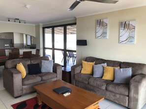 A modern living room with two sofas, a coffee table, and a dining area with chairs and a table. - Coral Towers (Cairns North)