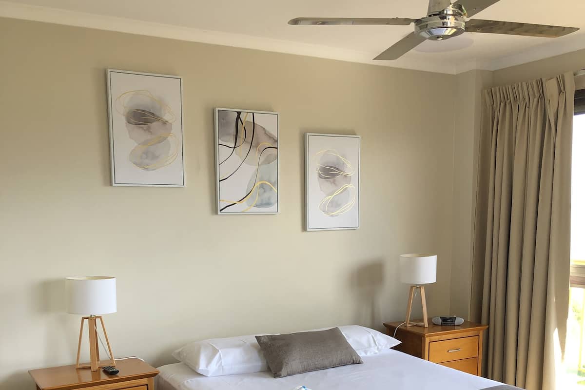 A hotel room with a bed, two bedside tables, a ceiling fan, and artwork on the wall.