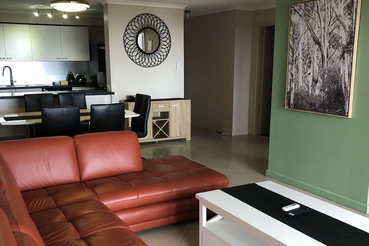 A modern living room with a sectional sofa, a white TV stand, and a dining area with a kitchen in the background.