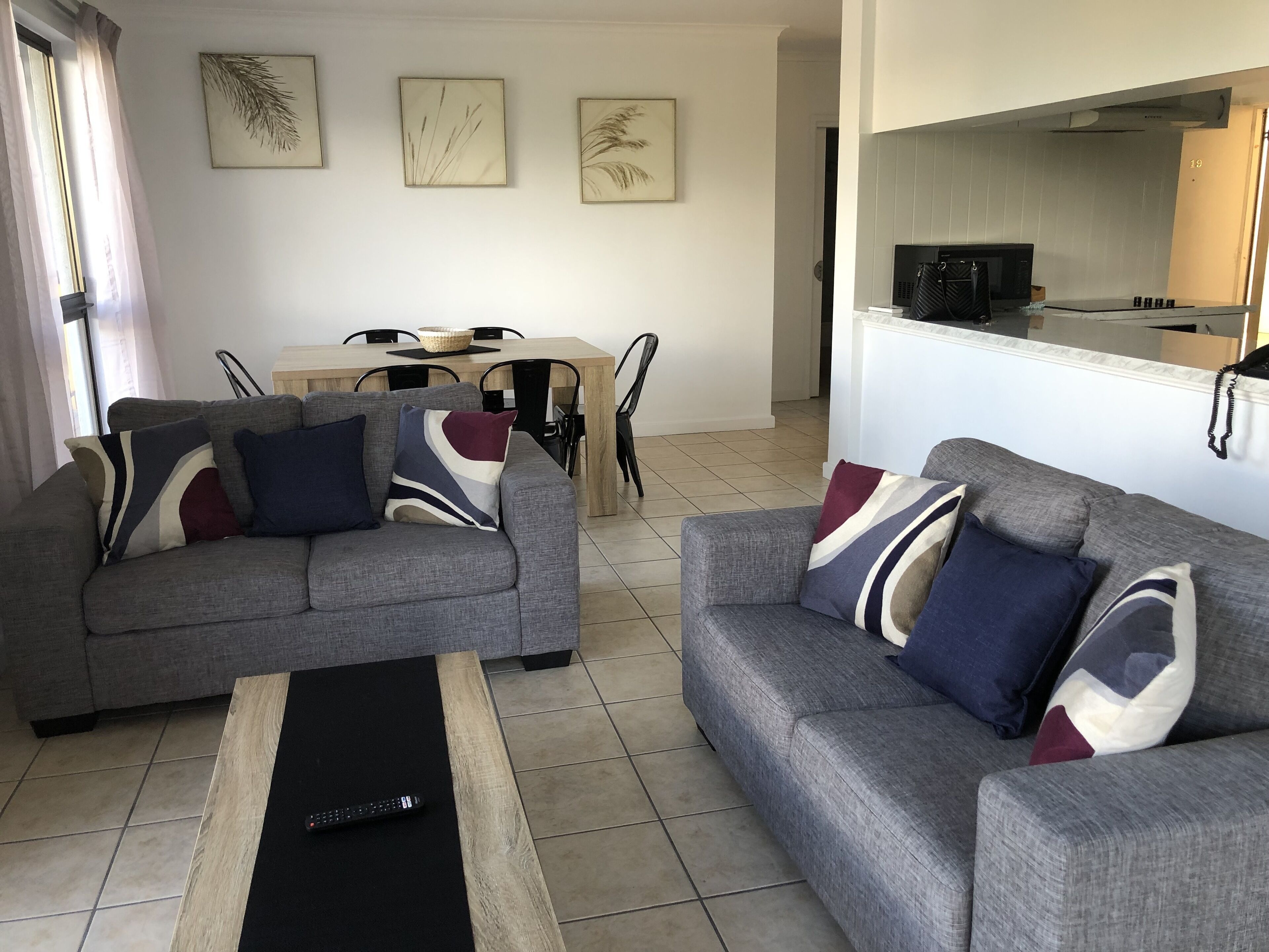 Una sala de estar con dos sofás grises, una mesa de centro negra y una zona de comedor con una mesa y sillas de madera.