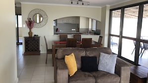 Una sala de estar con un sofá, una mesa de comedor y sillas. Hay una zona de cocina con armarios y una encimera.