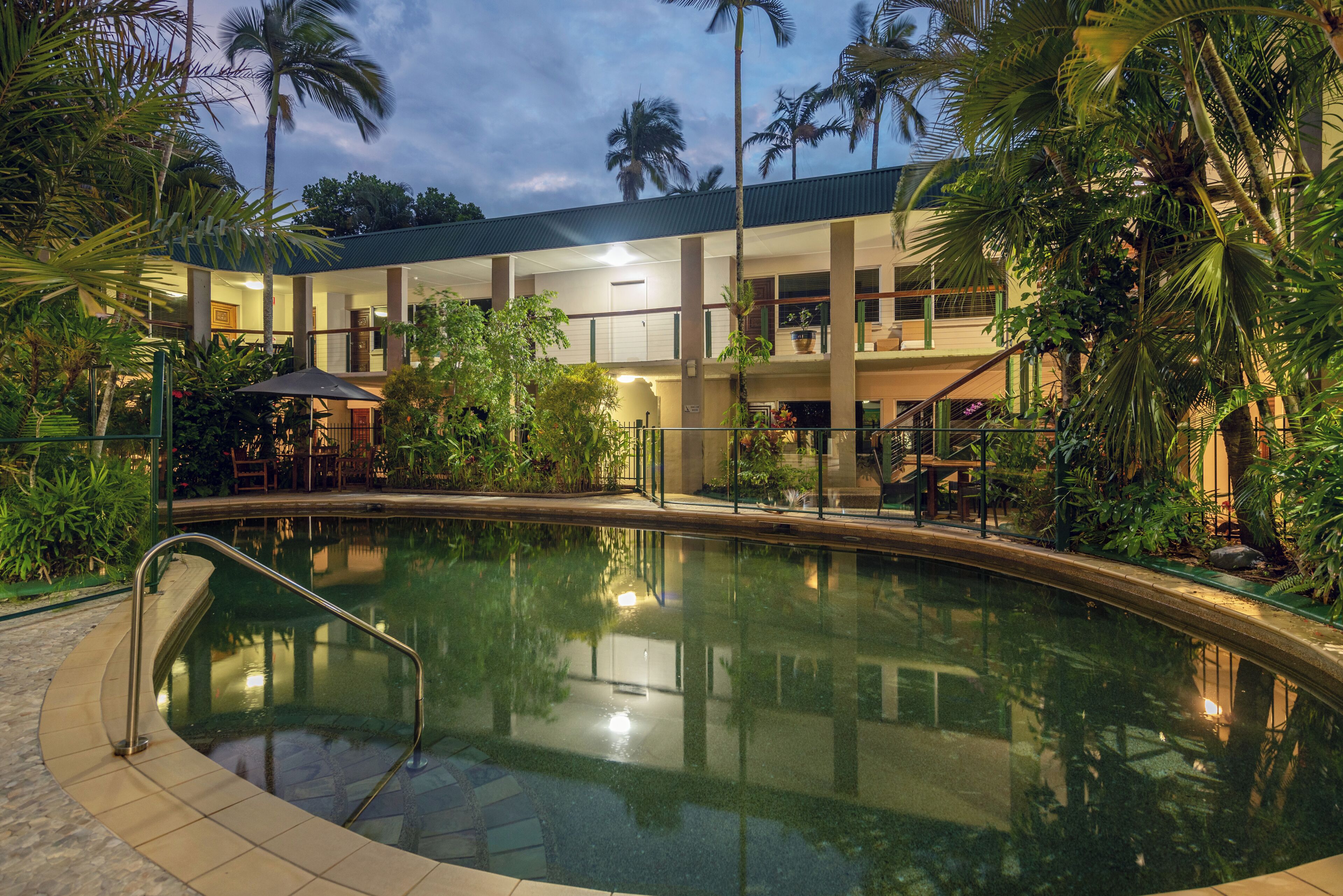 A swimming pool with a surrounding deck, palm trees, and a building with multiple floors and balconies.