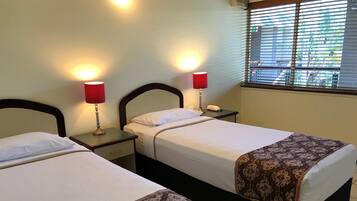 Two beds with headboards, bedside tables, lamps, and a window with blinds.