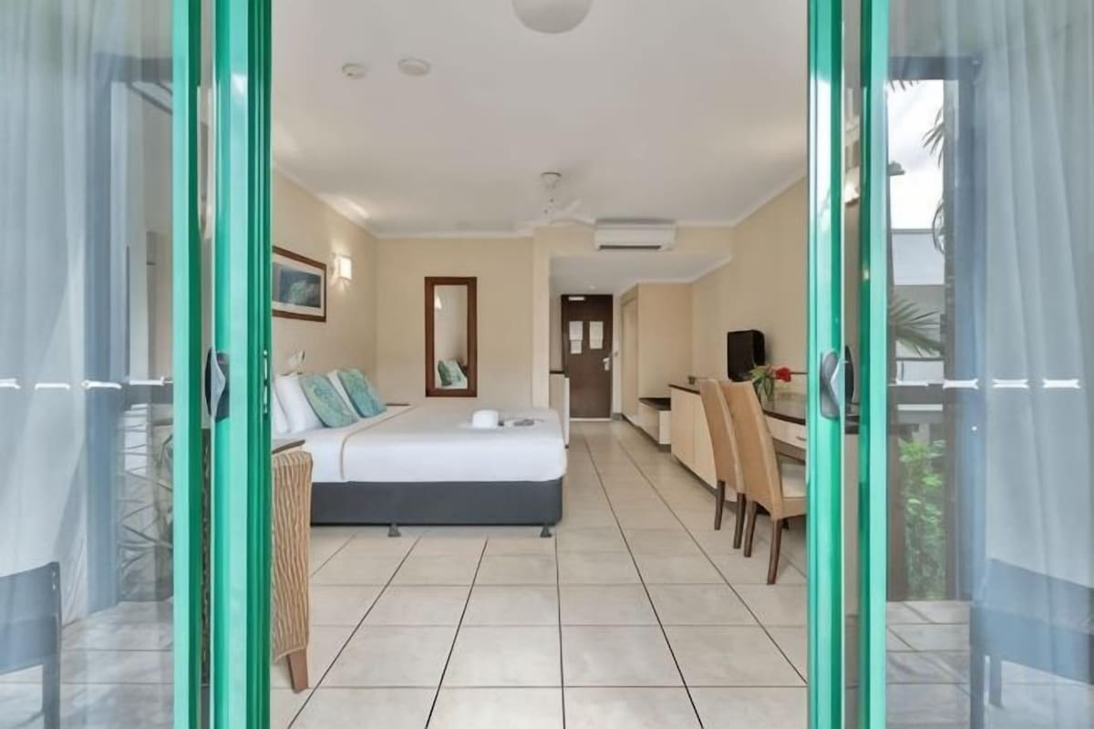 A hotel room with a bed, a desk, and a chair. There is a sliding glass door leading to an outdoor area.
