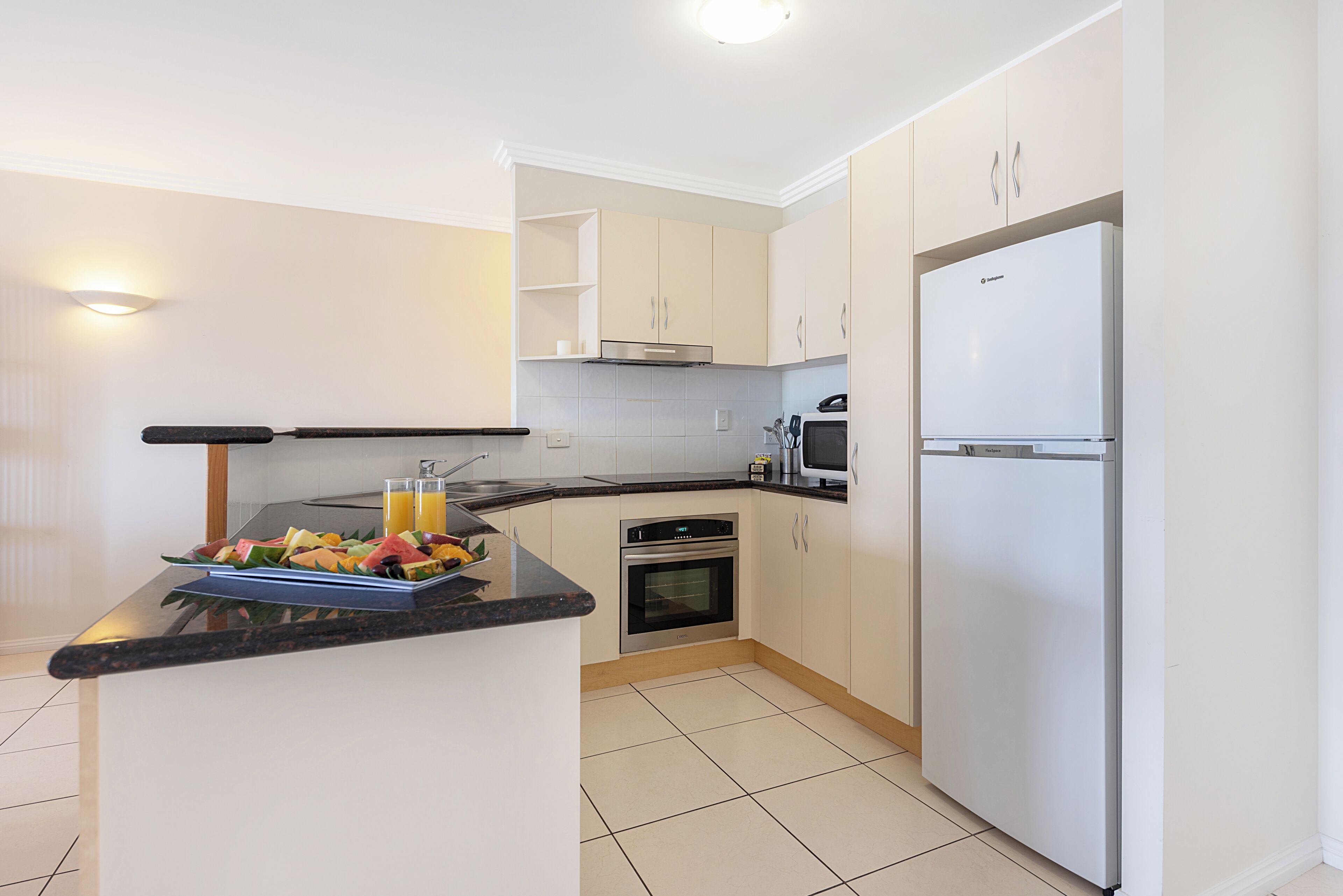 Una cocina moderna con horno empotrado, refrigerador y una encimera con frutero y vasos.