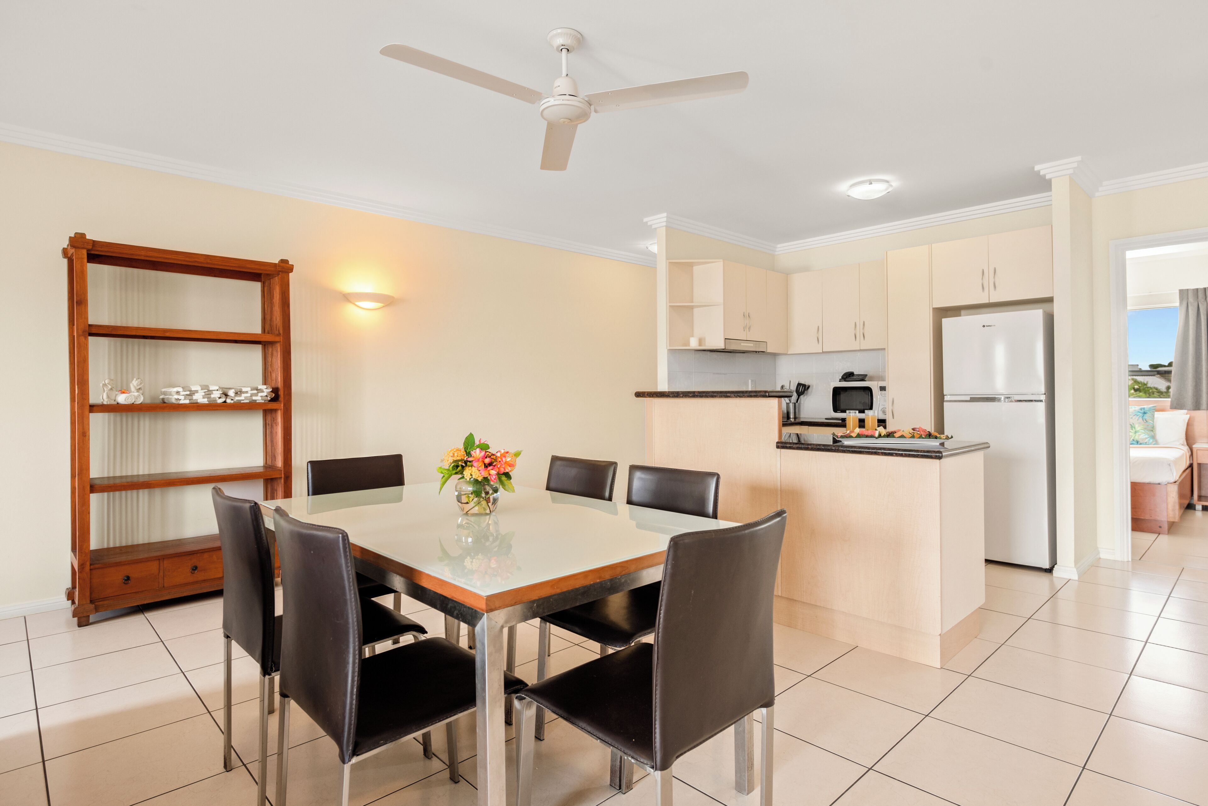 A modern kitchen with a dining area, a ceiling fan, and a wooden bookshelf.