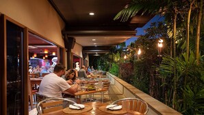 An outdoor dining area with tables and chairs, surrounded by greenery and a covered walkway. - Bay Village Tropical Retreat (Cairns North)