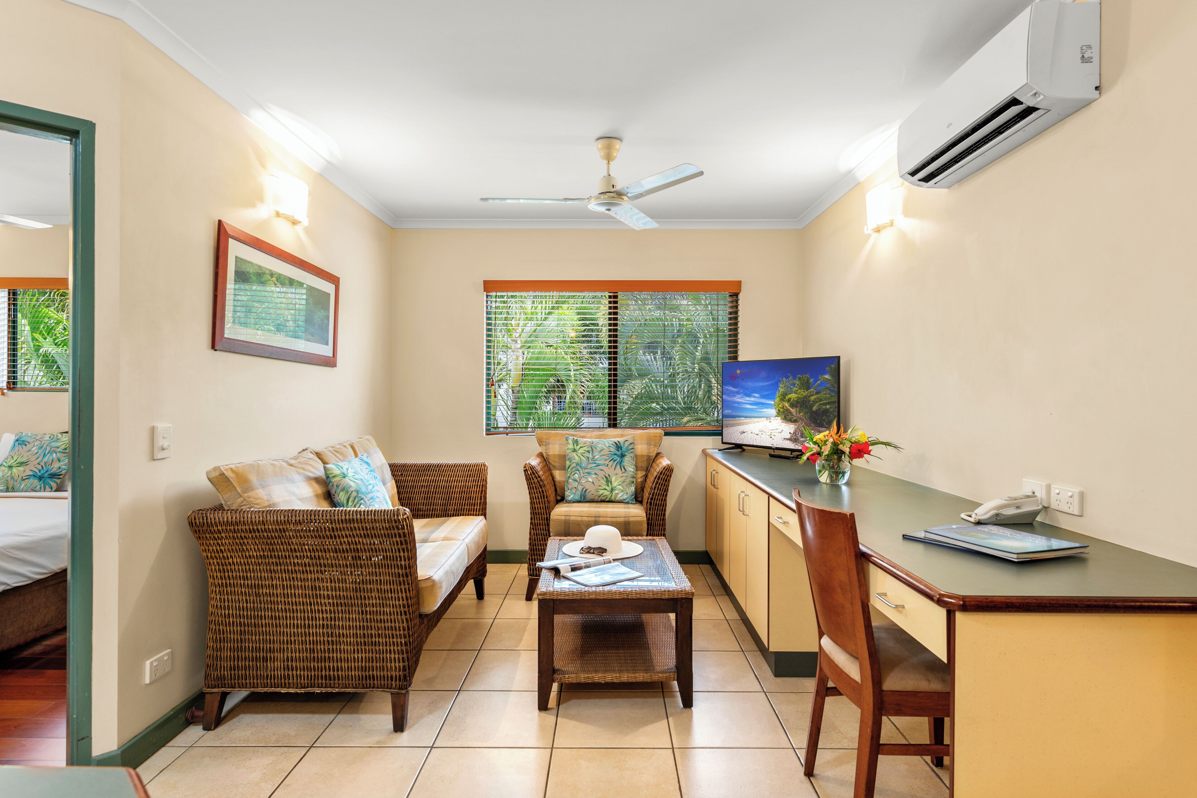 Una habitación con cama, una mesa de comedor, una silla, un sofá, un ventilador de techo, aire acondicionado y una ventana con persianas.