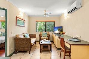 A room with a bed, a dining table, a chair, a sofa, a ceiling fan, an air conditioner, and a window with blinds.