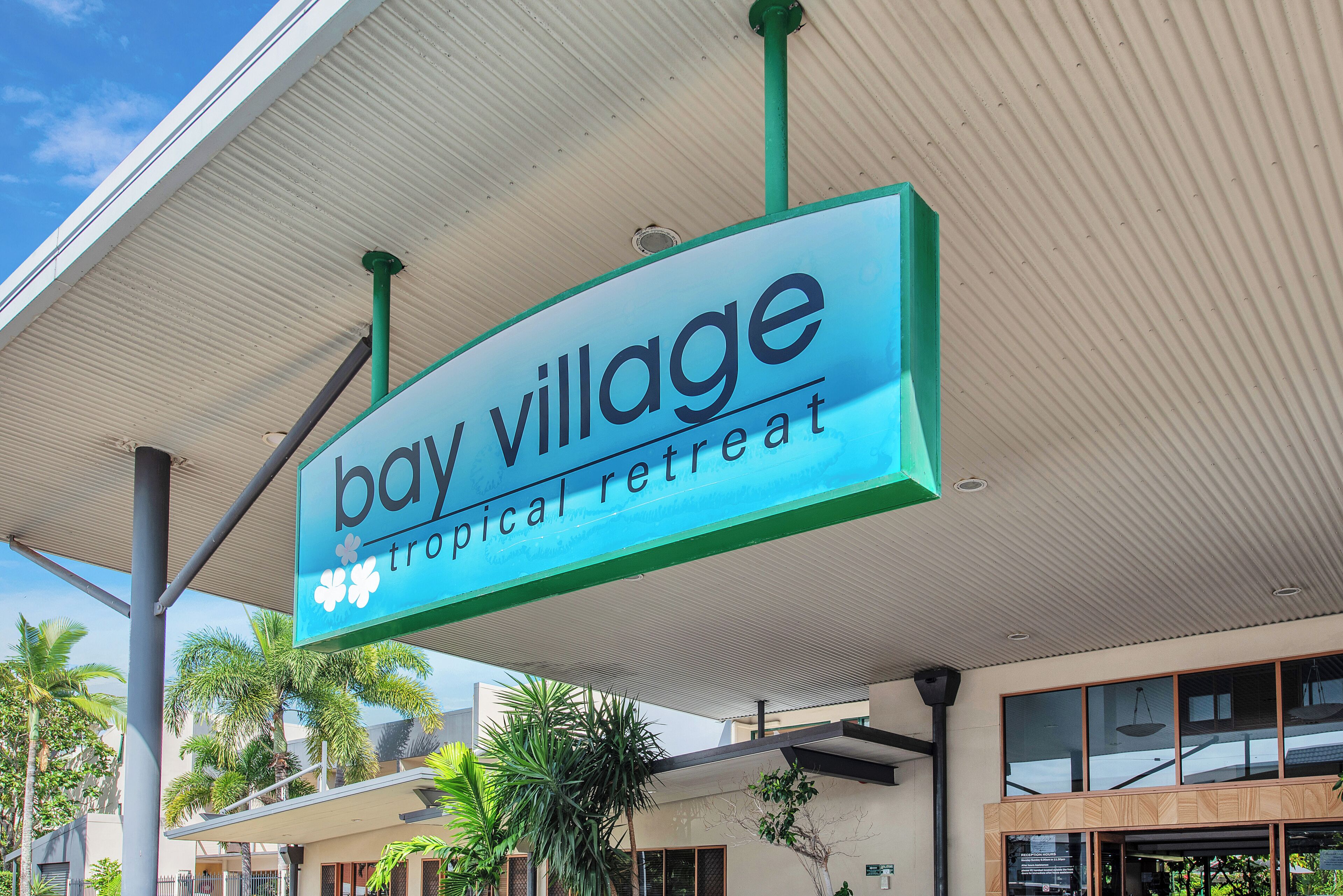 Skilt for 'bay village tropical retreat' med en moderne bygning i baggrunden.