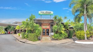 A hotel entrance with a sign reading 'bay village tropical retreat,' surrounded by lush greenery and palm trees. - Bay Village Tropical Retreat (Cairns North)
