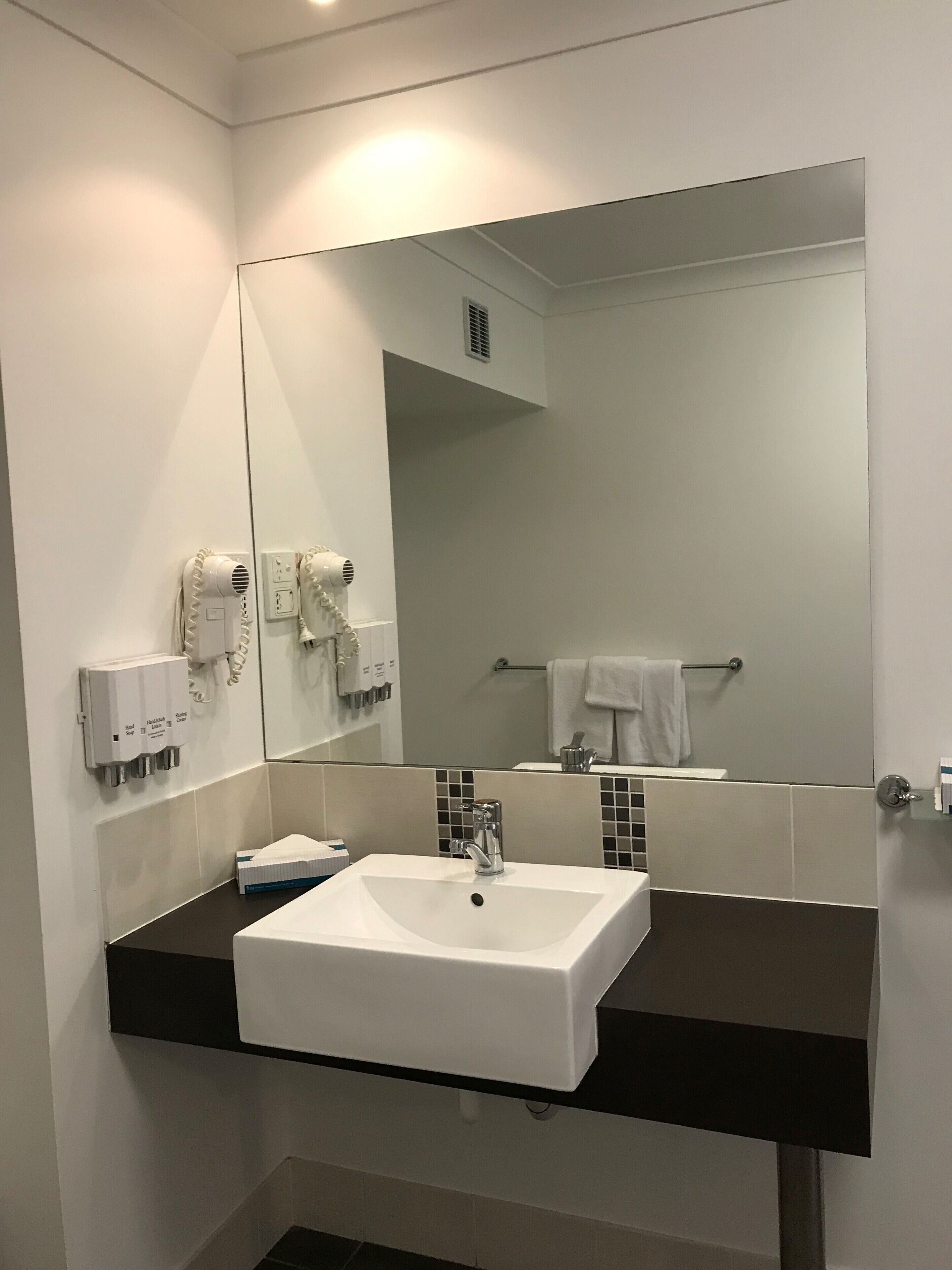 A bathroom with a white sink, a mirror, a towel rack, and a hand dryer.