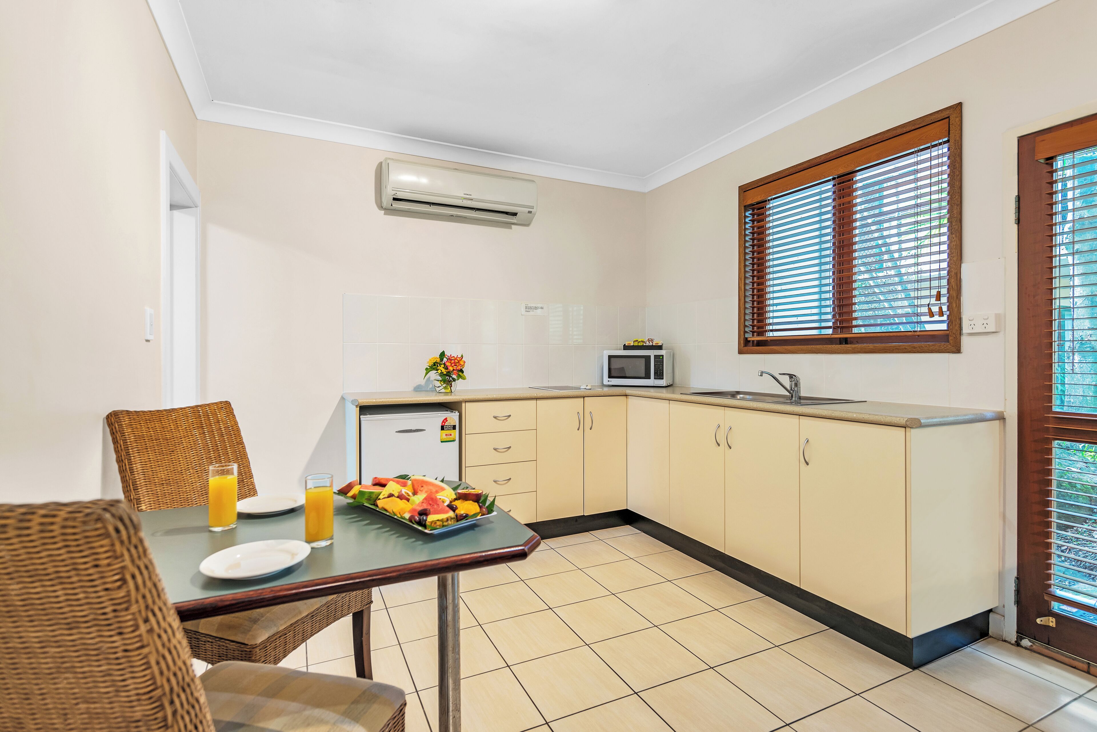 A kitchenette with a microwave, a sink, and a window with blinds.
