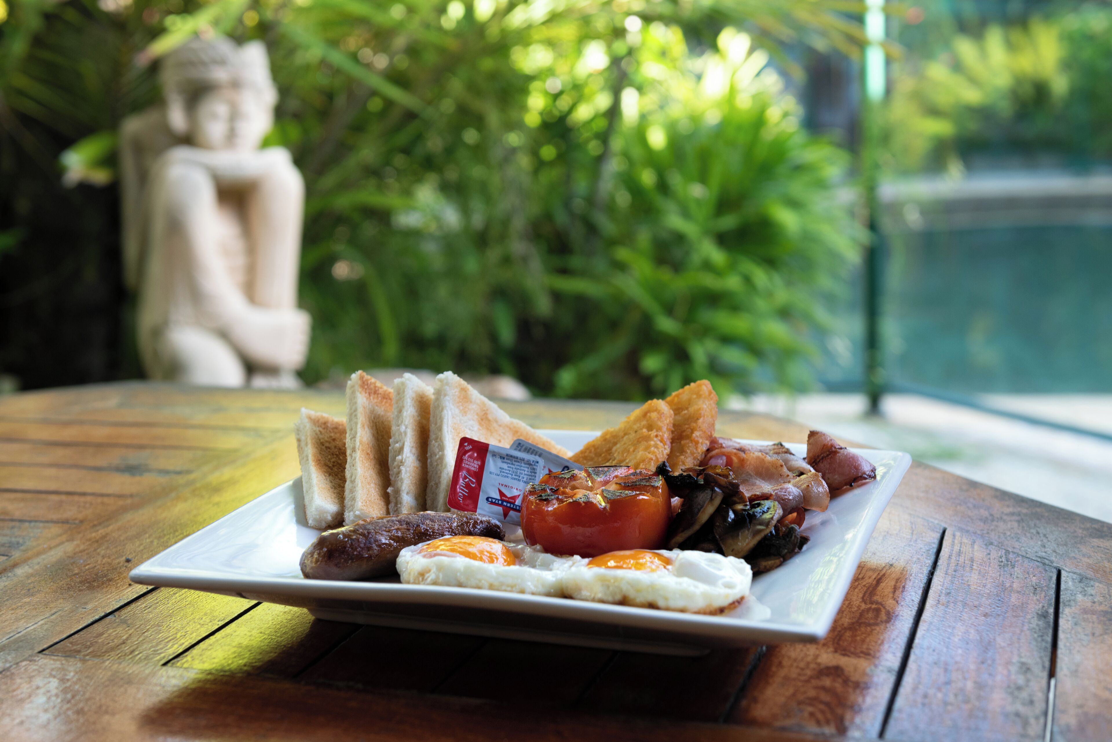 Un plato de desayuno con tostadas, huevos, salchichas y tomates sobre una mesa de madera.