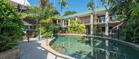 A pool area with lounge chairs, palm trees, and a building with multiple balconies.