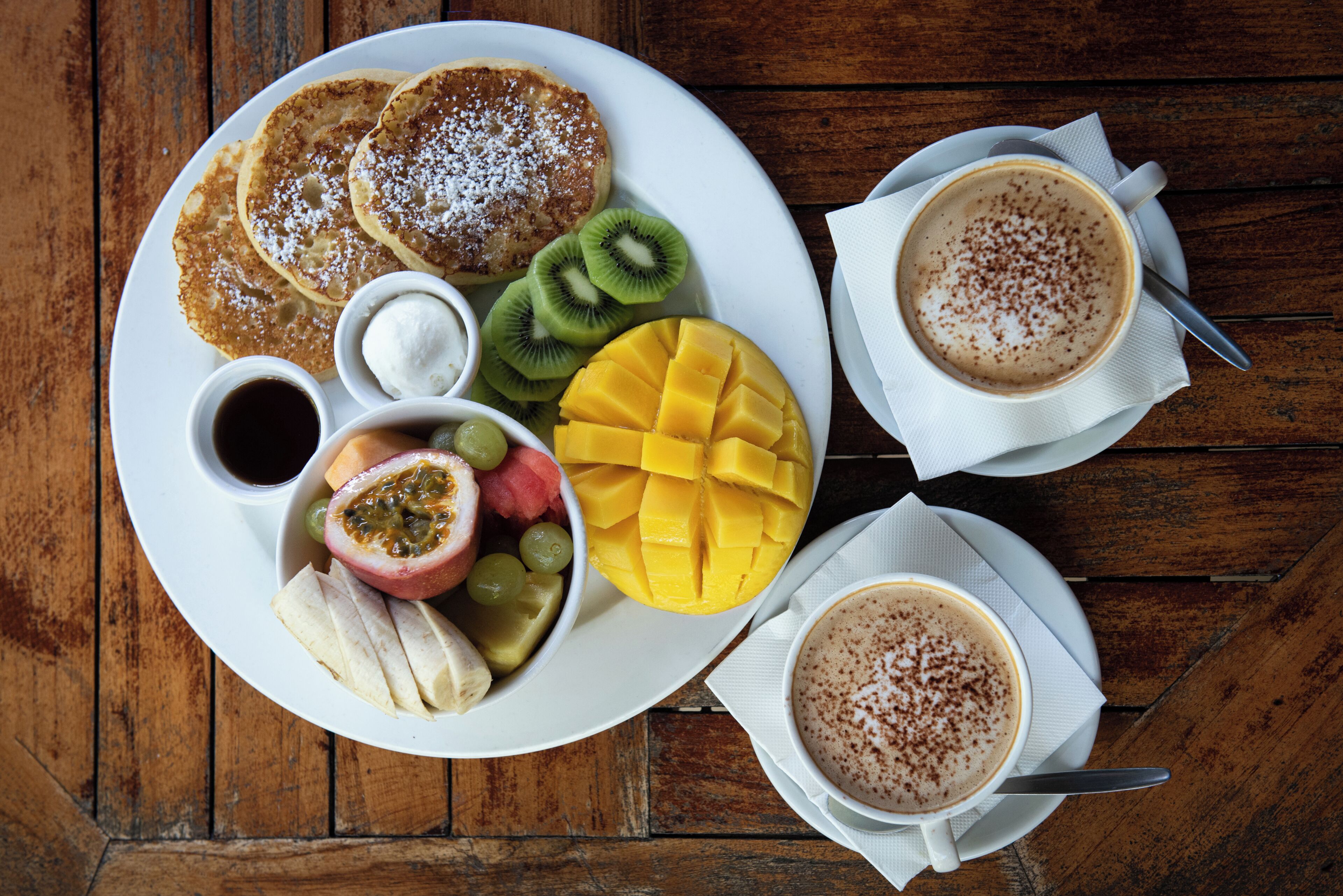 A breakfast plate with pancakes, fruit, and coffee on a wooden table.