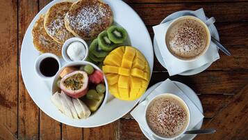 A breakfast plate with pancakes, fruit, and coffee on a wooden table.