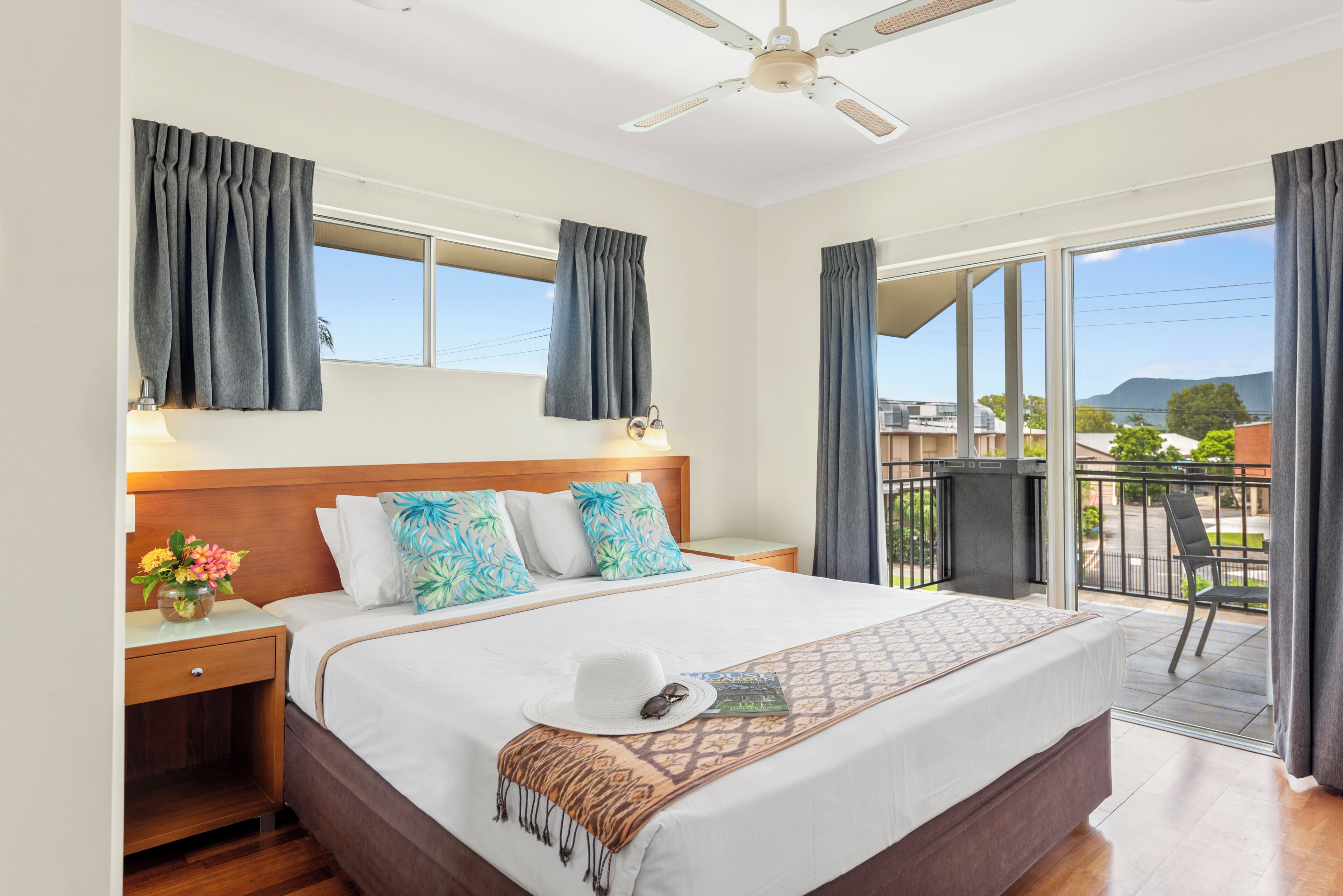 A hotel room with a bed, a nightstand, a window, a balcony, and a ceiling fan.