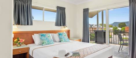 A hotel room with a bed, a nightstand, a window, a balcony, and a ceiling fan.