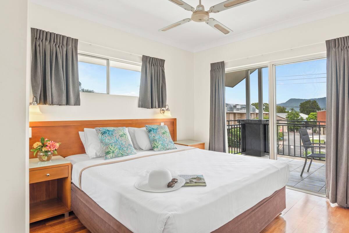 Une chambre d’hôtel avec un grand lit, un ventilateur de plafond, un balcon avec une chaise et une vue sur l’extérieur.