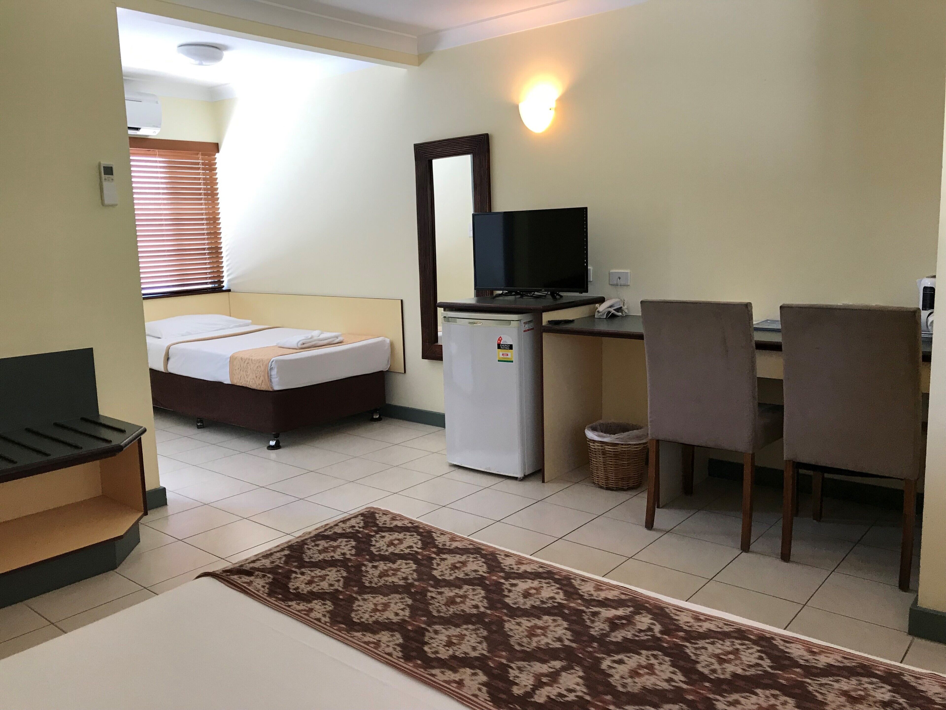 A hotel room with a bed, desk, chair, television, and a small refrigerator.