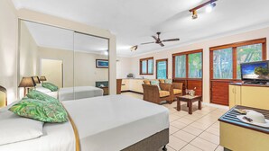 A hotel room with a bed, a desk, a chair, a TV, and a ceiling fan. - Bay Village Tropical Retreat (Cairns North)