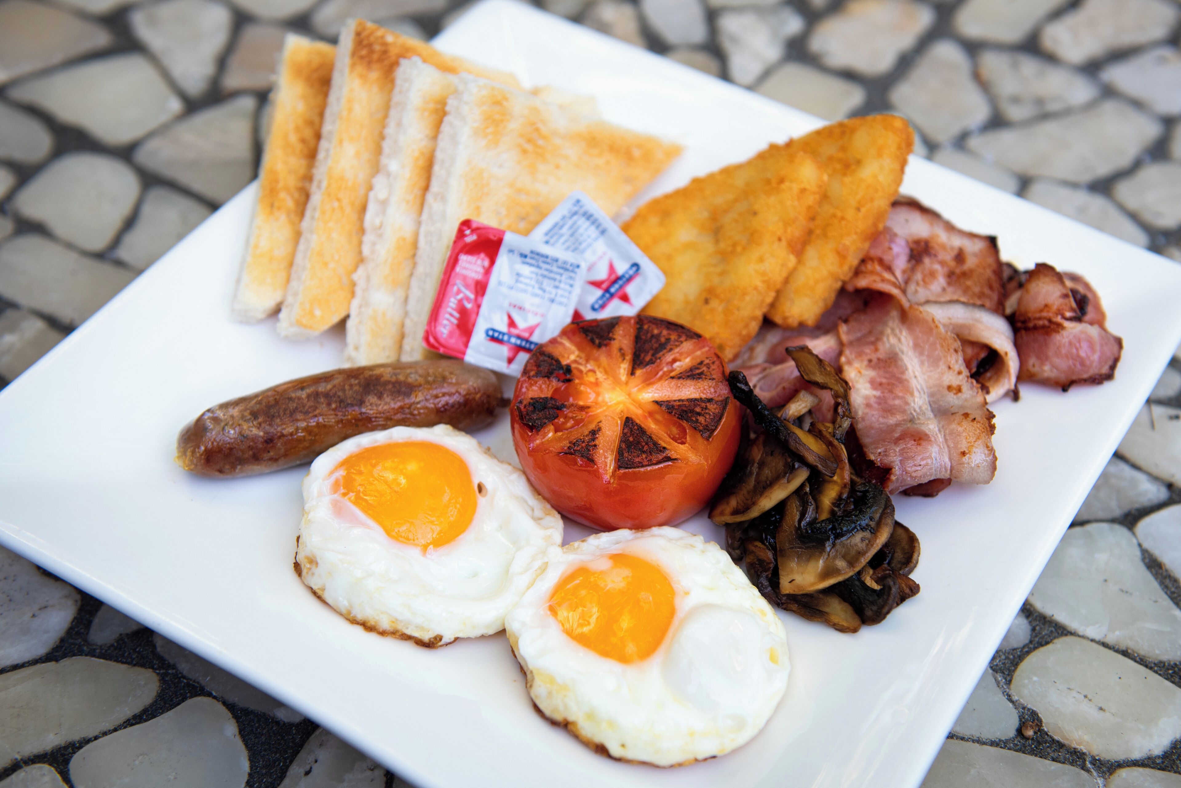 Un plato de desayuno con huevos, tocino, salchichas, tostadas y un tomate a la parrilla.