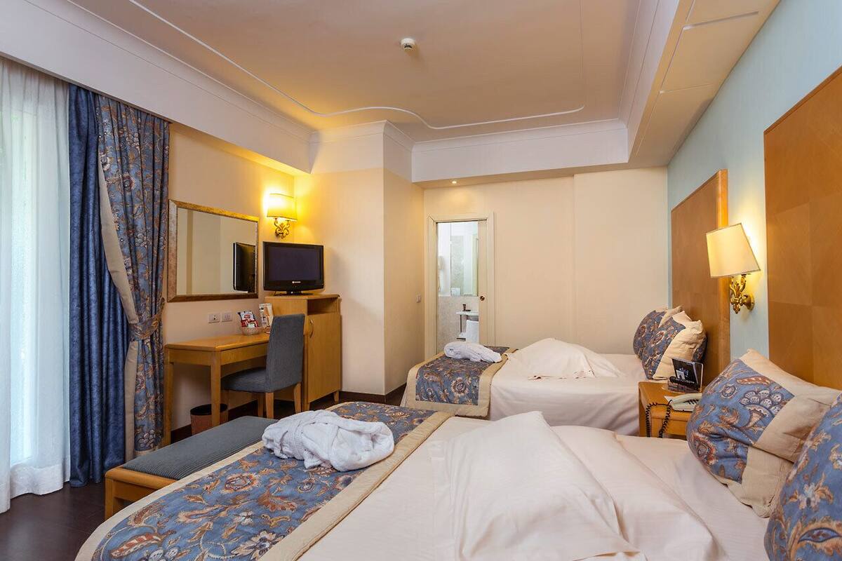Una habitación de hotel con dos camas, un escritorio, una silla, un televisor y la puerta del baño.