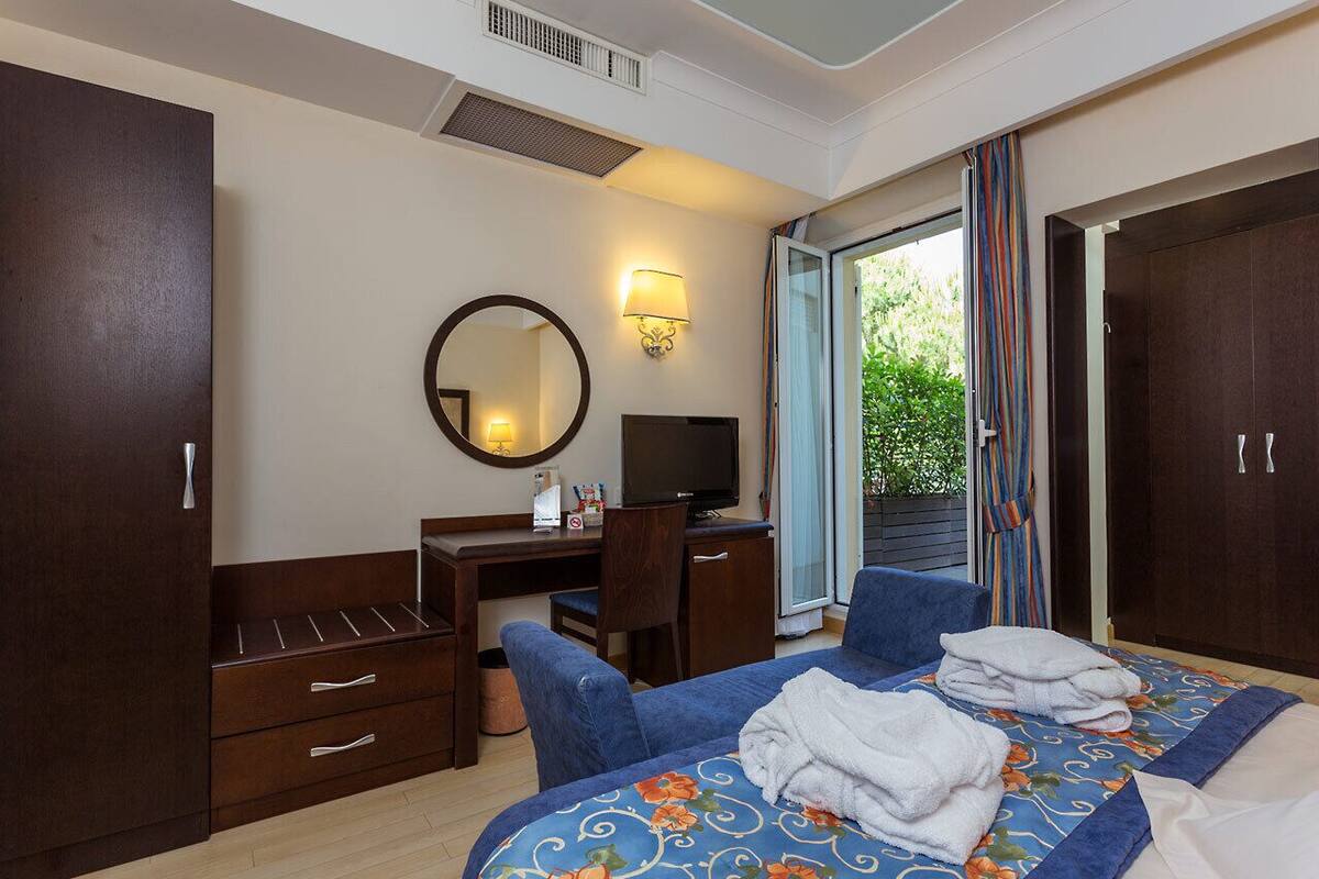 Una habitación de hotel con cama, escritorio, silla, televisor y armario.