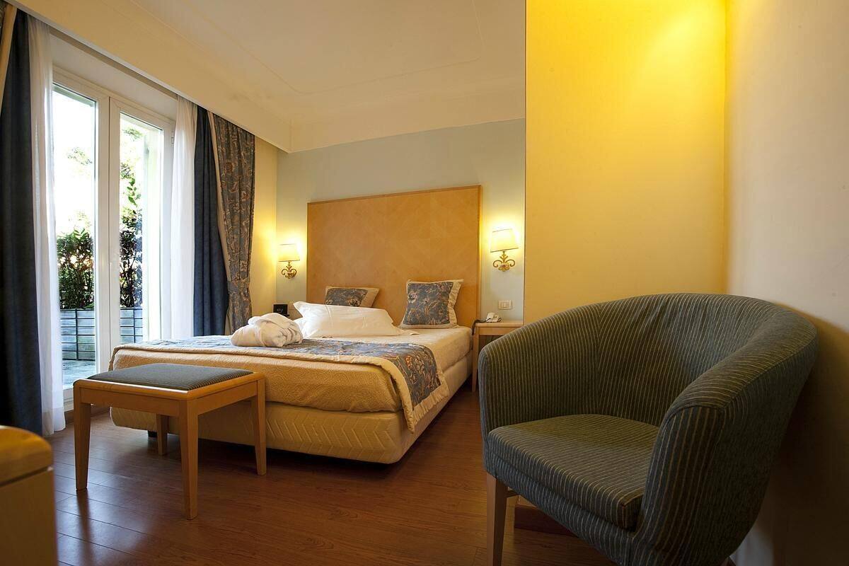 Una habitación de hotel con cama, una silla, una mesita y una ventana con cortinas.