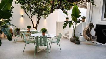 Un patio con una mesa redonda y sillas, rodeado de macetas con plantas y una silla colgante.