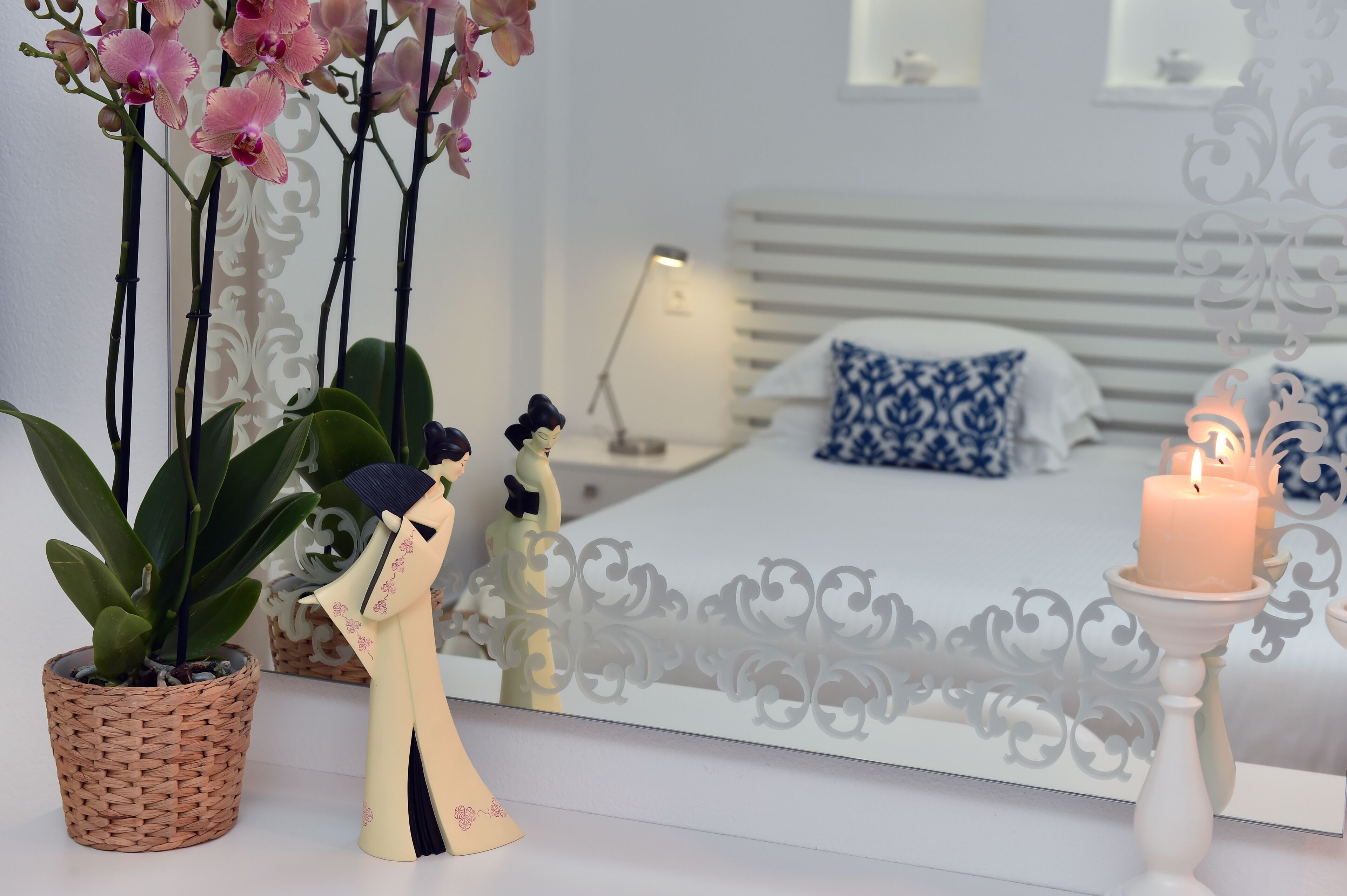 A bedroom with a bed, bedside table, lamp, decorative pillows, a mirror, and a lit candle.