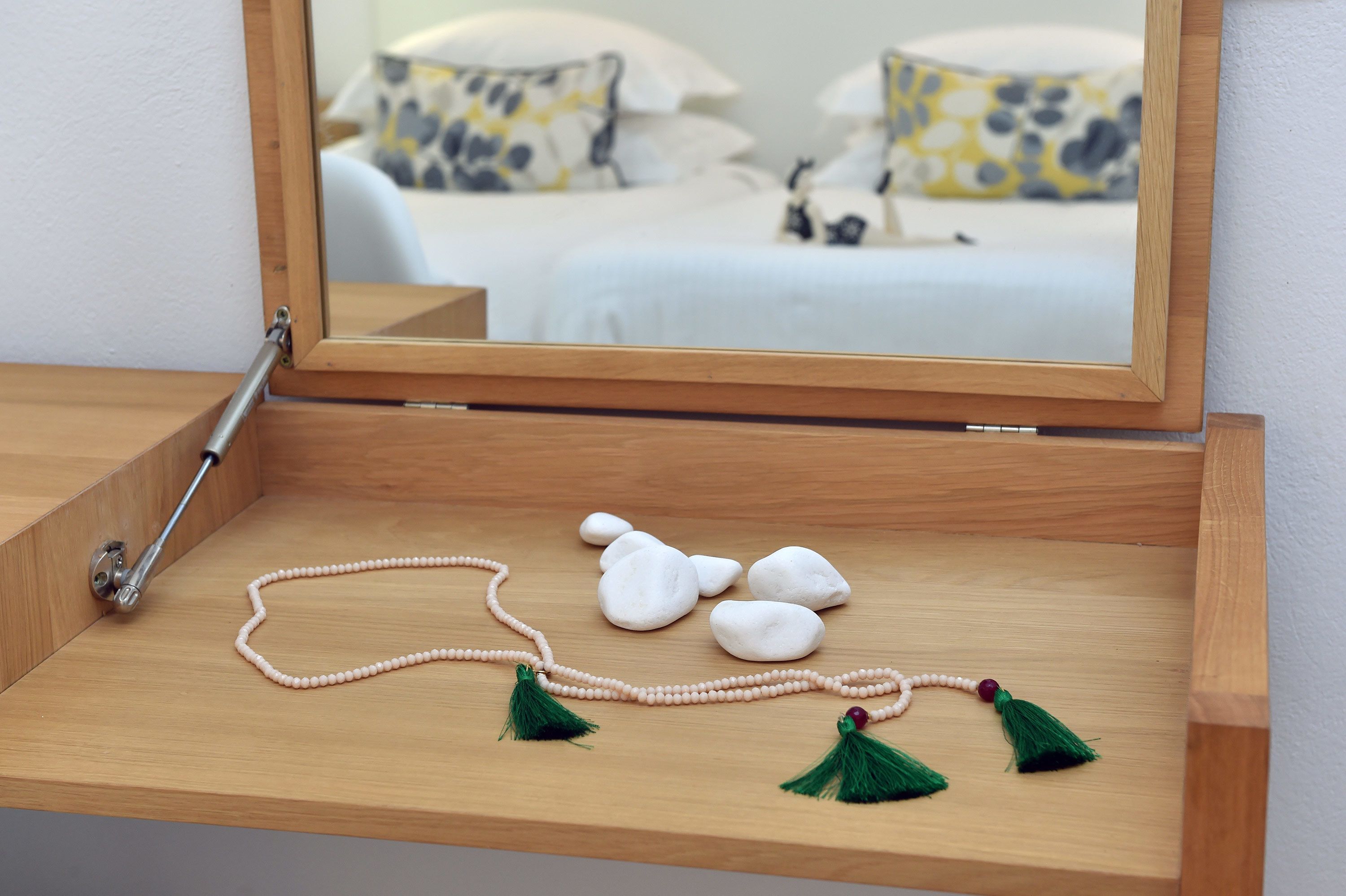 Una estantería de madera con un espejo, una guirnalda de cuentas y piedras lisas.