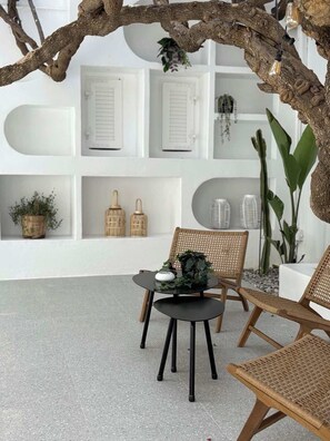 A seating area with wicker chairs, a round table, and shelves with decorative items. - Apollon Boutique Hotel (Paros)
