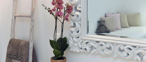 A bathroom with a white vanity, a mirror with ornate white frame, a towel rack with a towel, and a potted orchid.